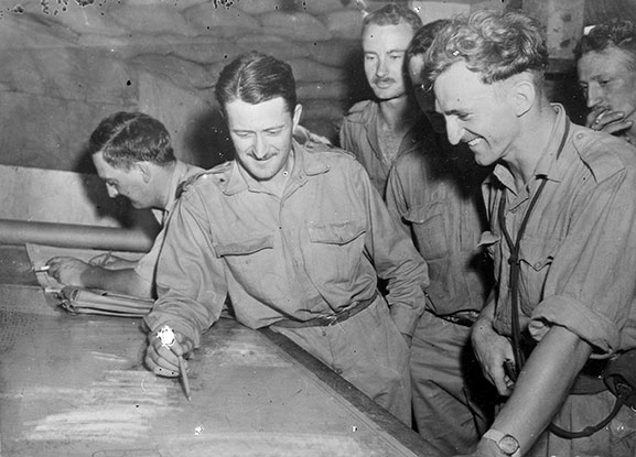 Image ref: PR2998©RNZAF Official George Gudsell (right foreground) discussing tactics in an operations room on Guadalcanal in 1942. 