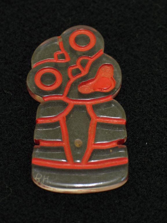 Tiki pendant made from clear plexiglass (perspex).  Carved details have been highlighted with red paint.  Made while with Royal New Zealand Air Force No. 12 Servicing Unit at Henderson Field, Guadalcanal.