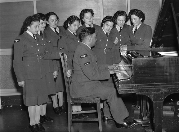 Women's Auxiliary Air Force Māori choir group gathered around a piano, 1943. Image ref PR2194, RNZAF Official.