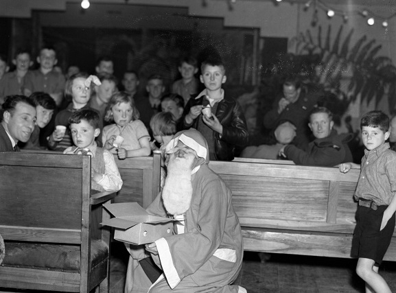 Santa Claus with a box of presents at a children's Christmas party, Anderson Park Camp, Wellington, 1944. Image ref PR4487, RNZAF Official.