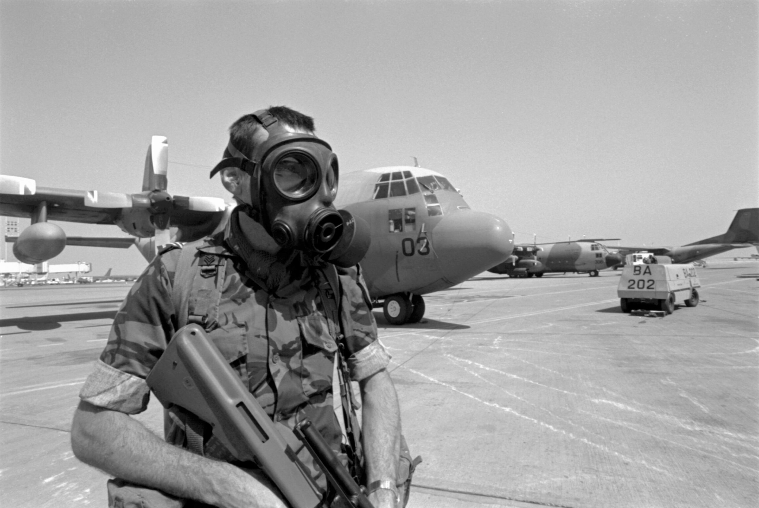 Sergeant Phil Lane, wearing a gas mask, on security duty on the tarmac in front of No. 40 Squadron Hercules NZ7003. Riyadh, Saudi Arabia, Feb-Mar 1991. Image ref PD14-2-91, RNZAF Official.